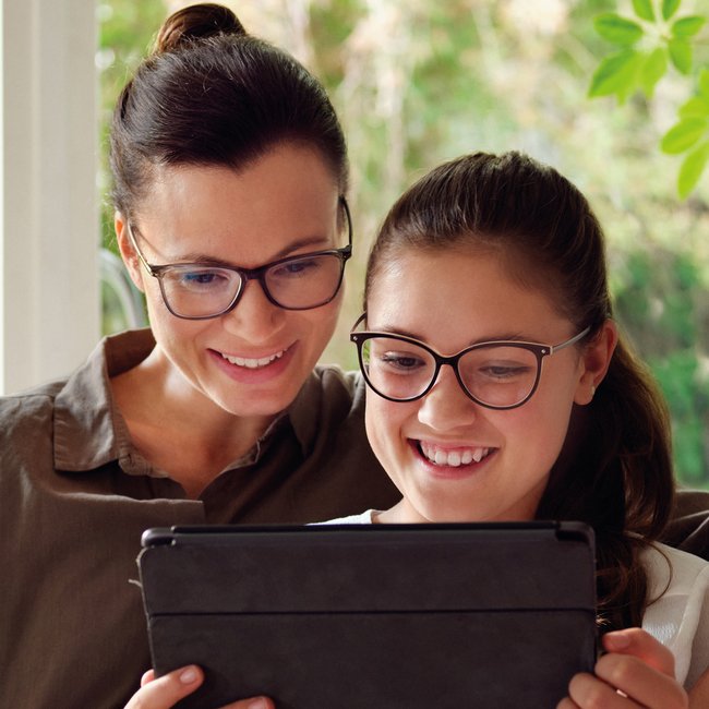 Mujer e hija usando tablet juntas en casa, representando el uso de lentes MyCon para controlar la miopía infantil